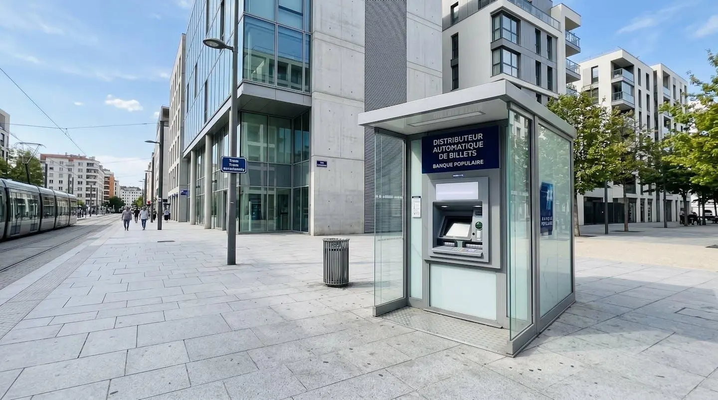 Distributeur automatique bancaire moderne installé dans un espace urbain européen contemporain lumineux, architecture récente en arrière-plan